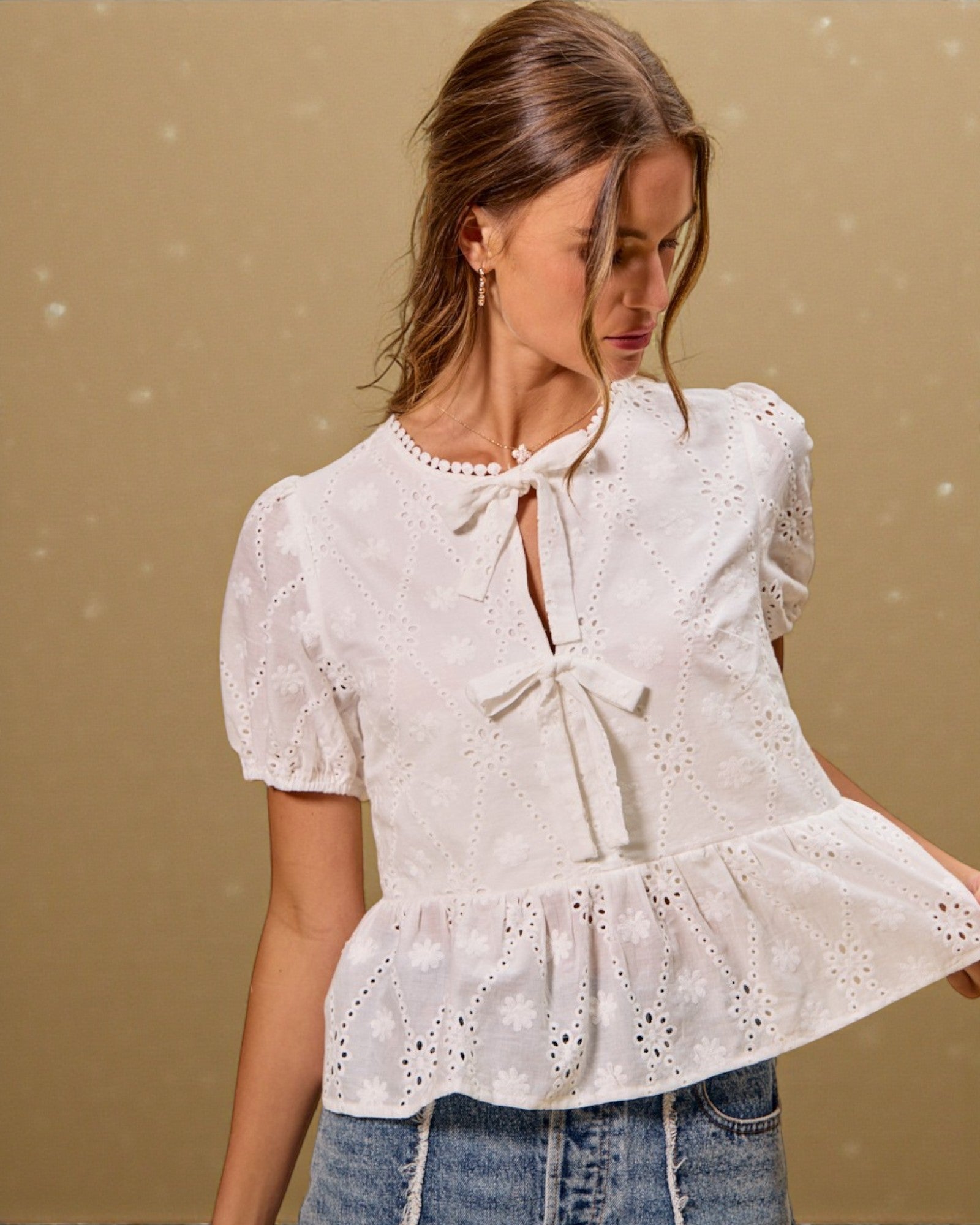 Woman wearing a white blouse with a tie detail against a beige background