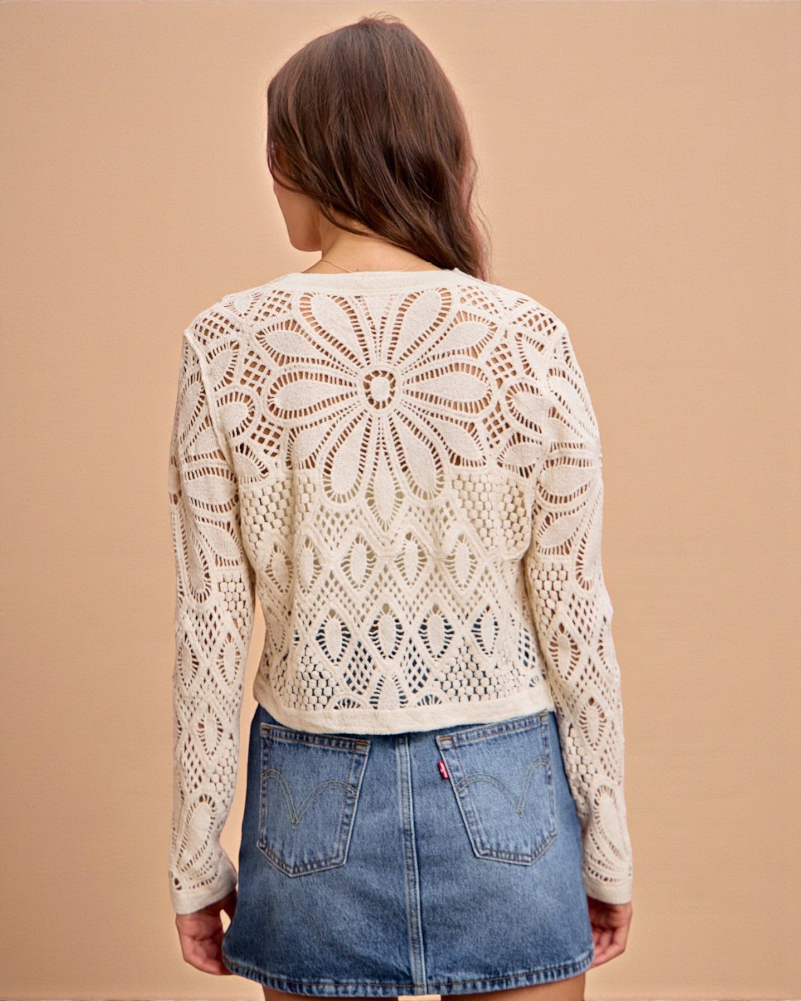 Woman wearing a beige lace top and denim shorts on a beige background