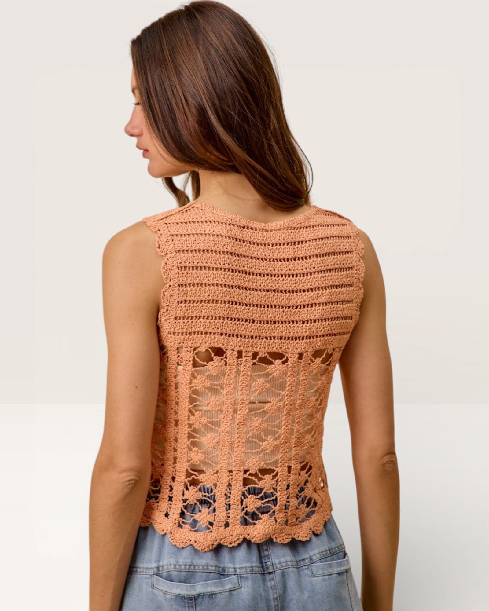 Woman wearing a peach-colored crochet top against a plain background