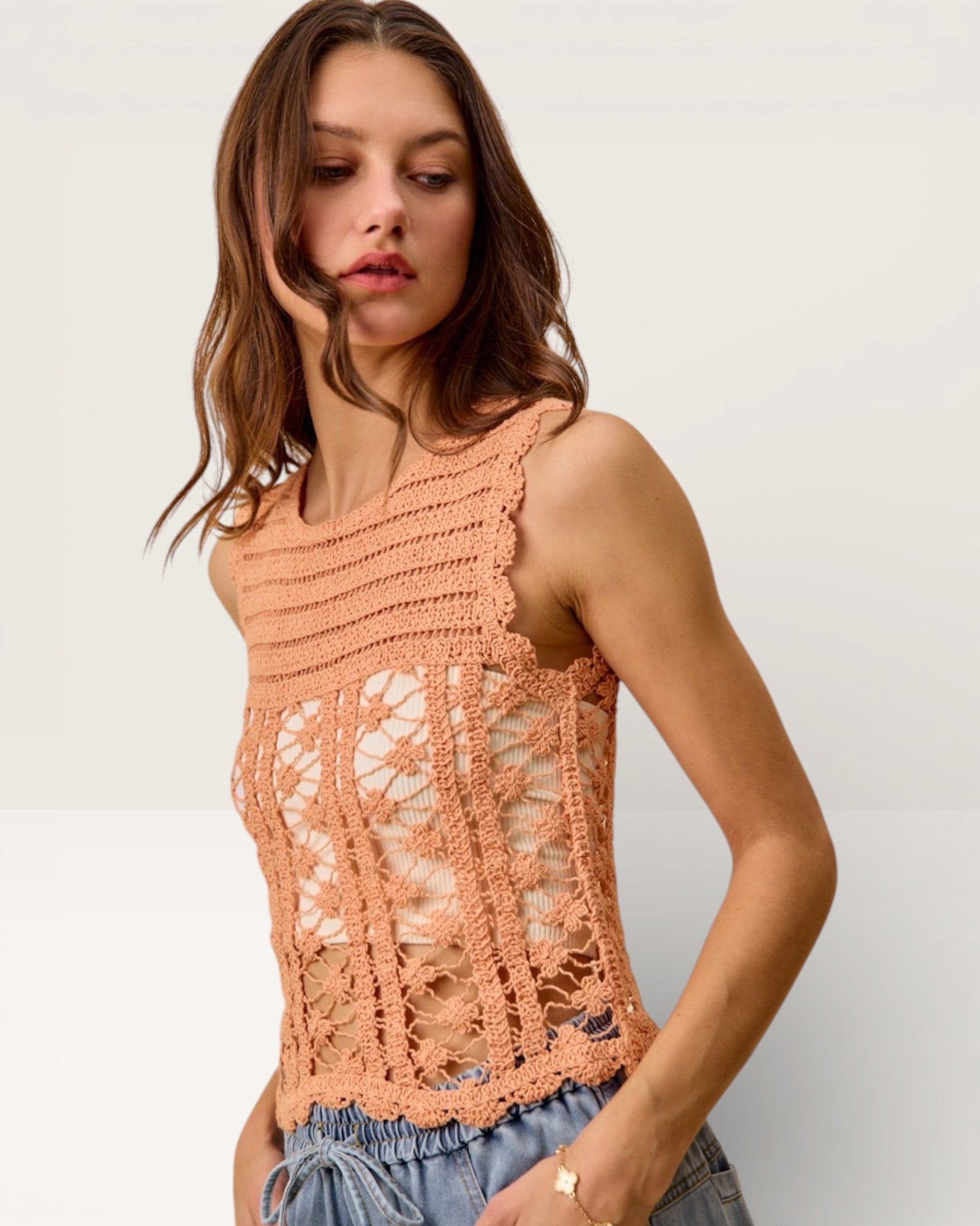 Woman wearing a peach-colored crochet top against a plain background