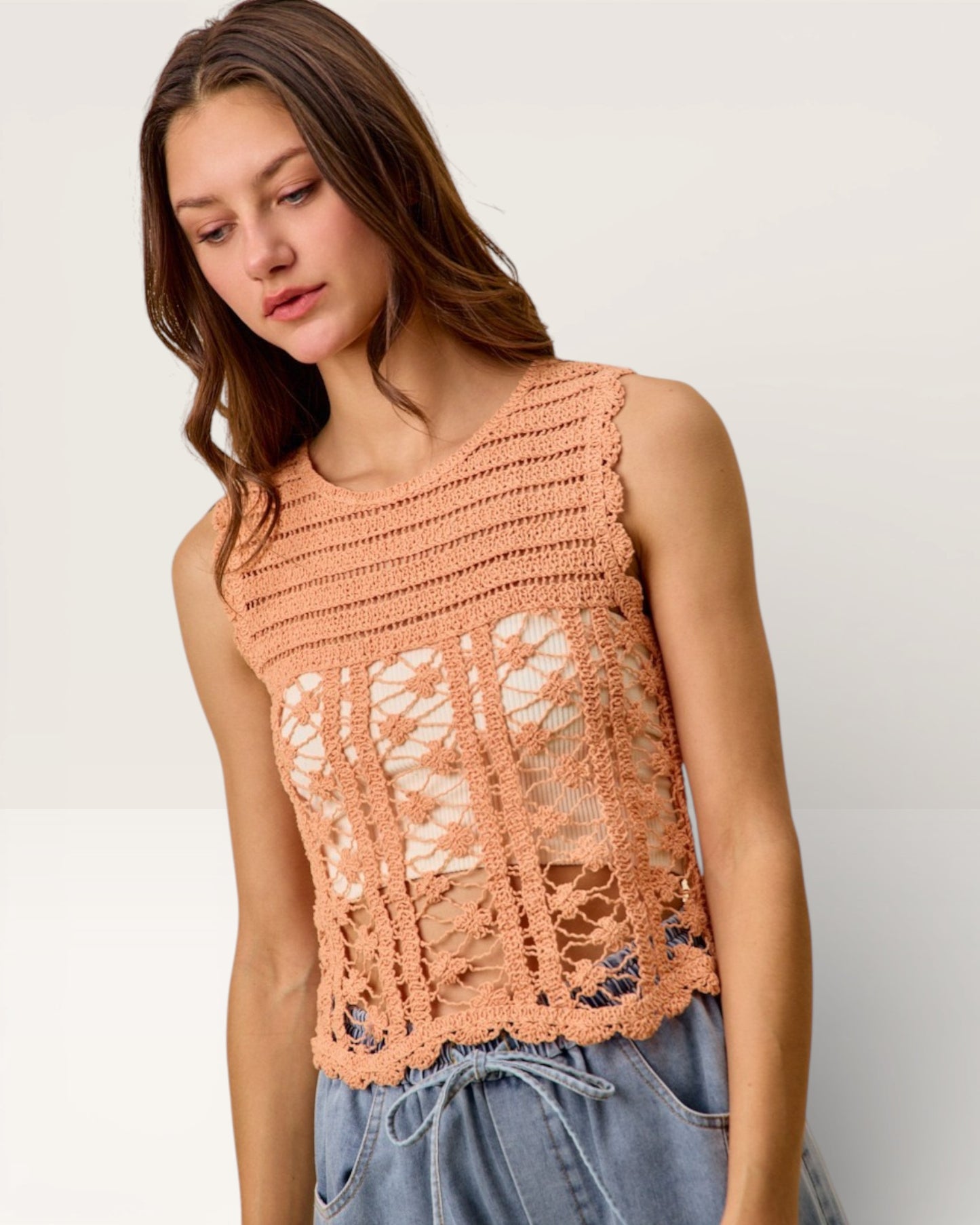 Woman wearing a peach-colored crochet top against a white background