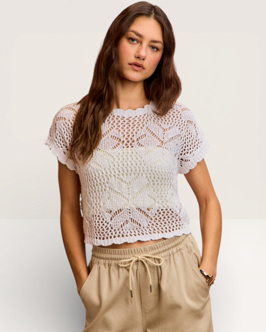 Woman wearing a white lace top and beige pants against a plain background