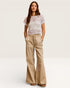 Woman wearing a white lace top and beige flared pants on a plain background