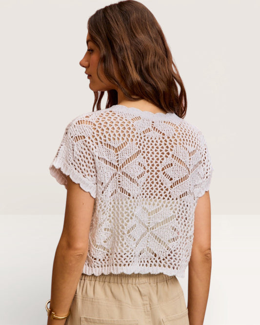 Woman wearing a white crochet top against a plain background
