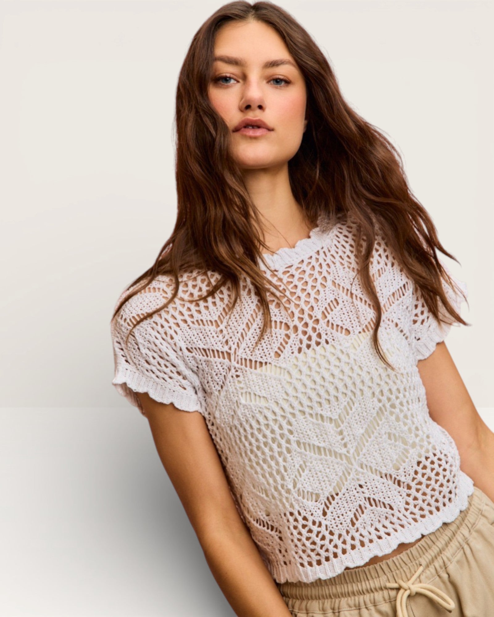 Woman wearing a white lace top against a plain background