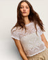 Woman wearing a white lace top against a plain background