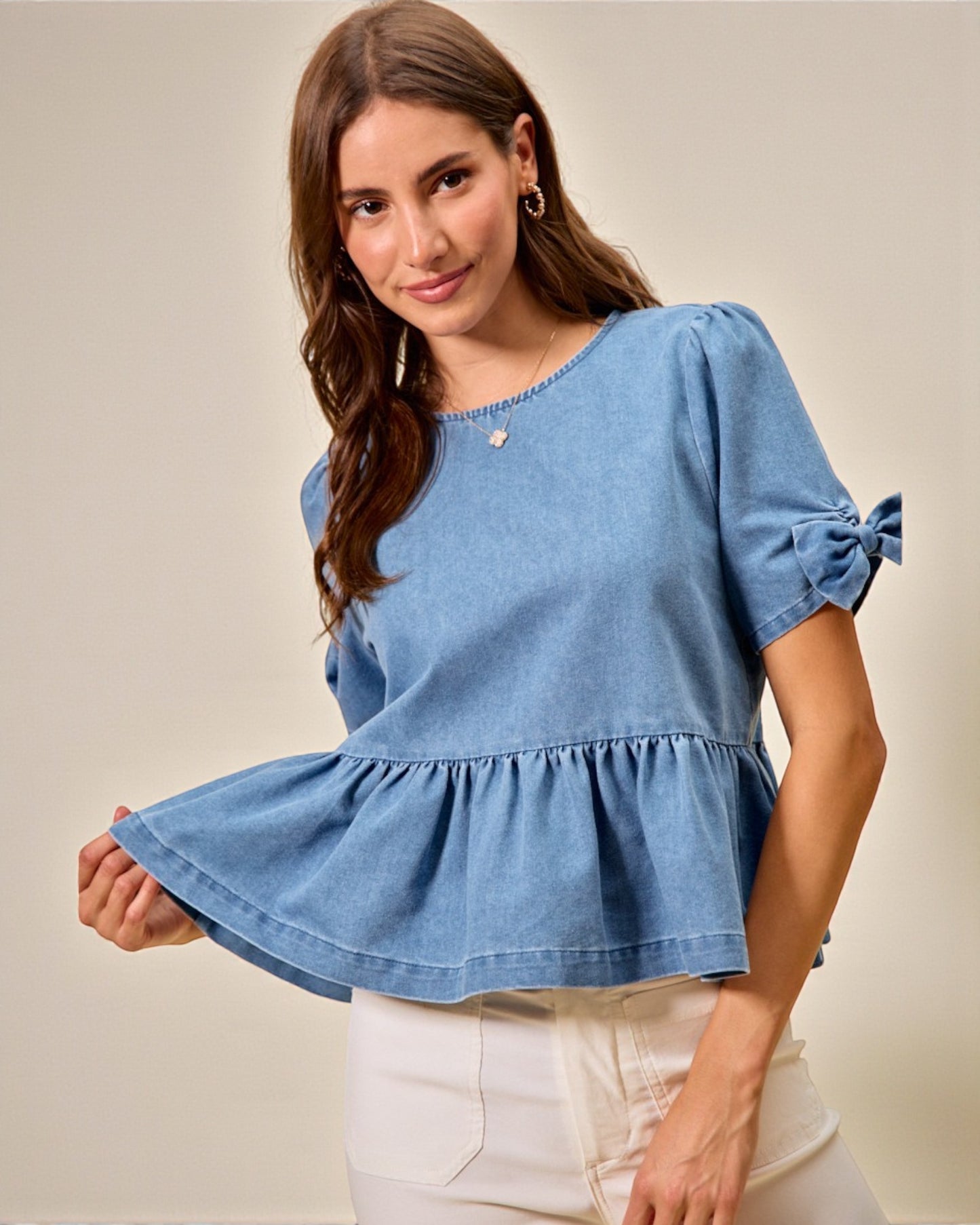 Woman wearing a blue denim top with ruffled sleeves against a beige background
