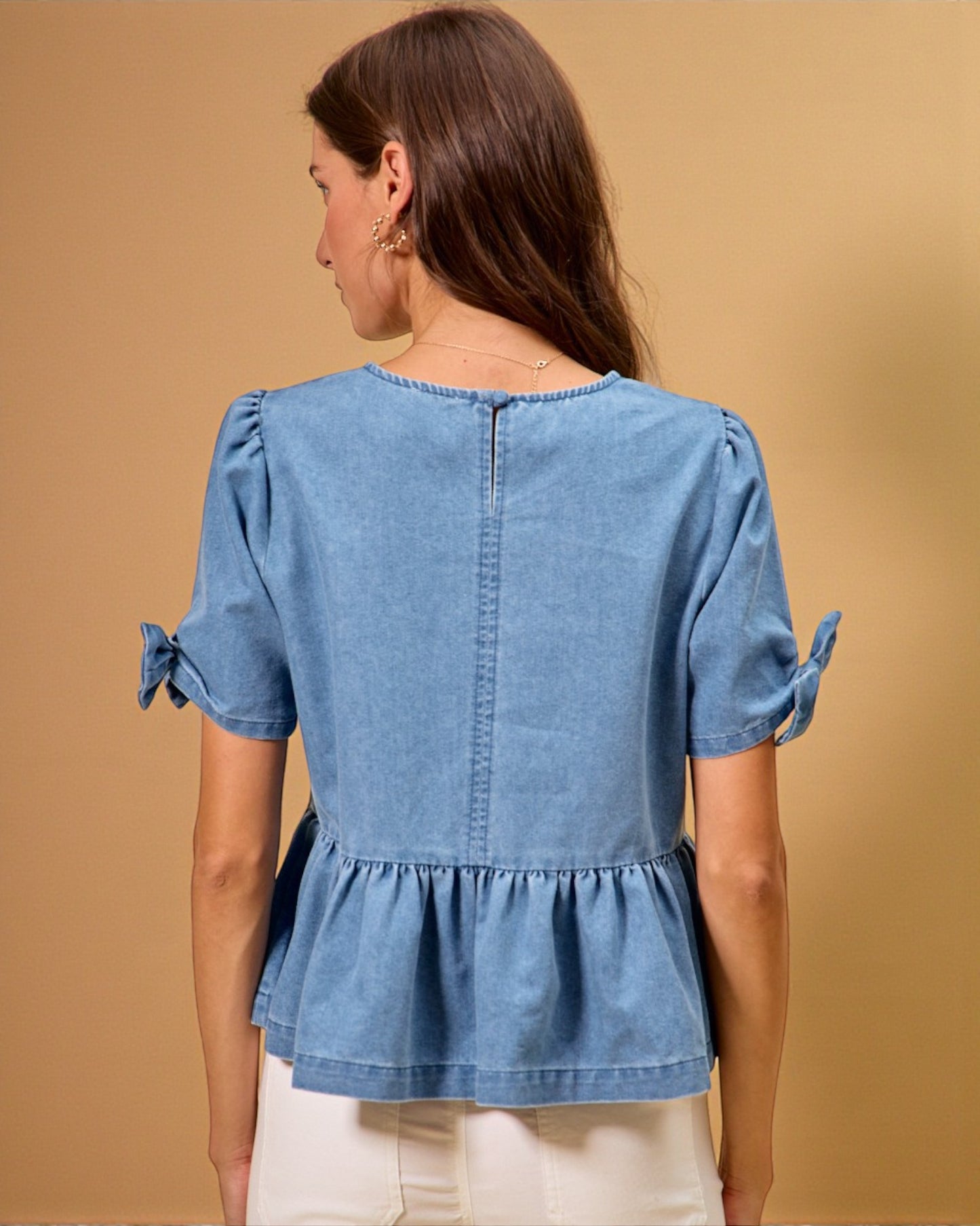 Woman wearing a blue denim top with bow sleeves against a beige background
