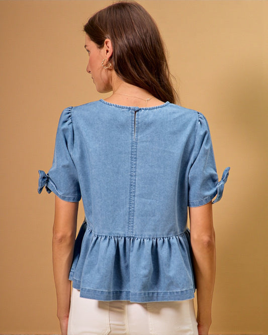 Woman wearing a blue denim top with bow sleeves against a beige background
