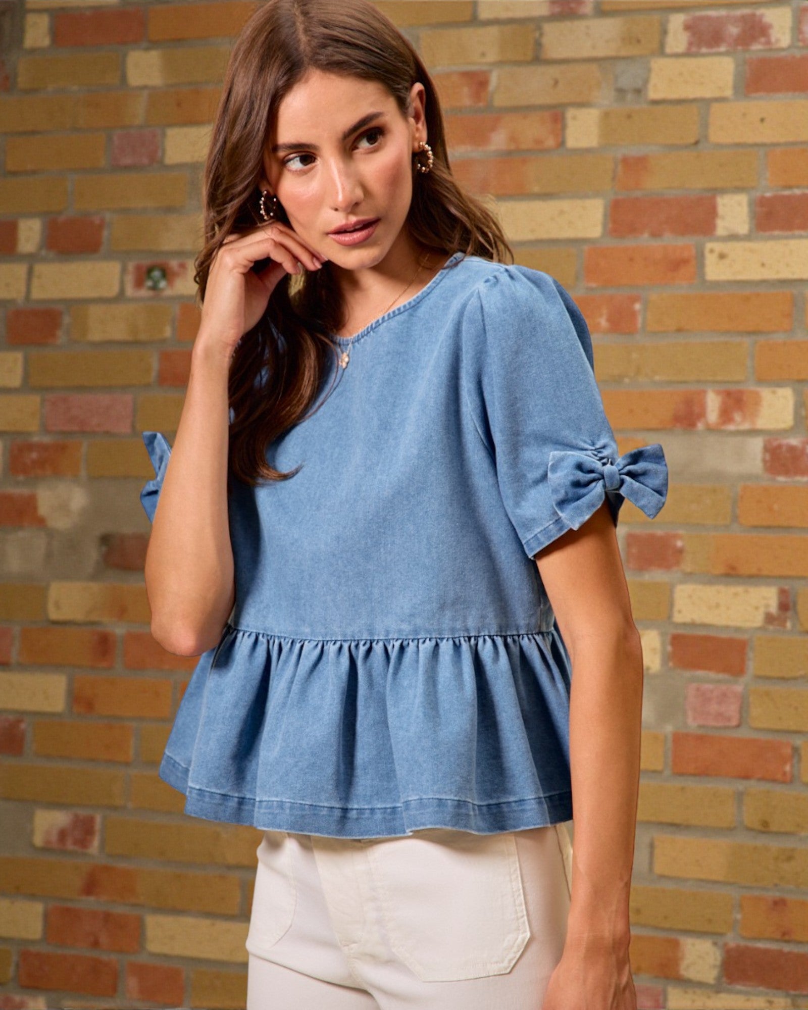 Woman wearing a blue denim top with ruffled sleeves against a brick wall.