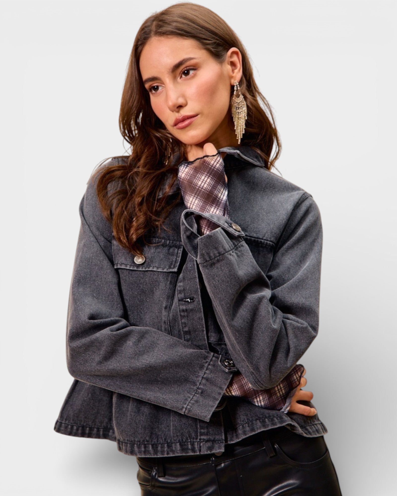 Woman wearing a denim jacket over a plaid shirt on a plain background