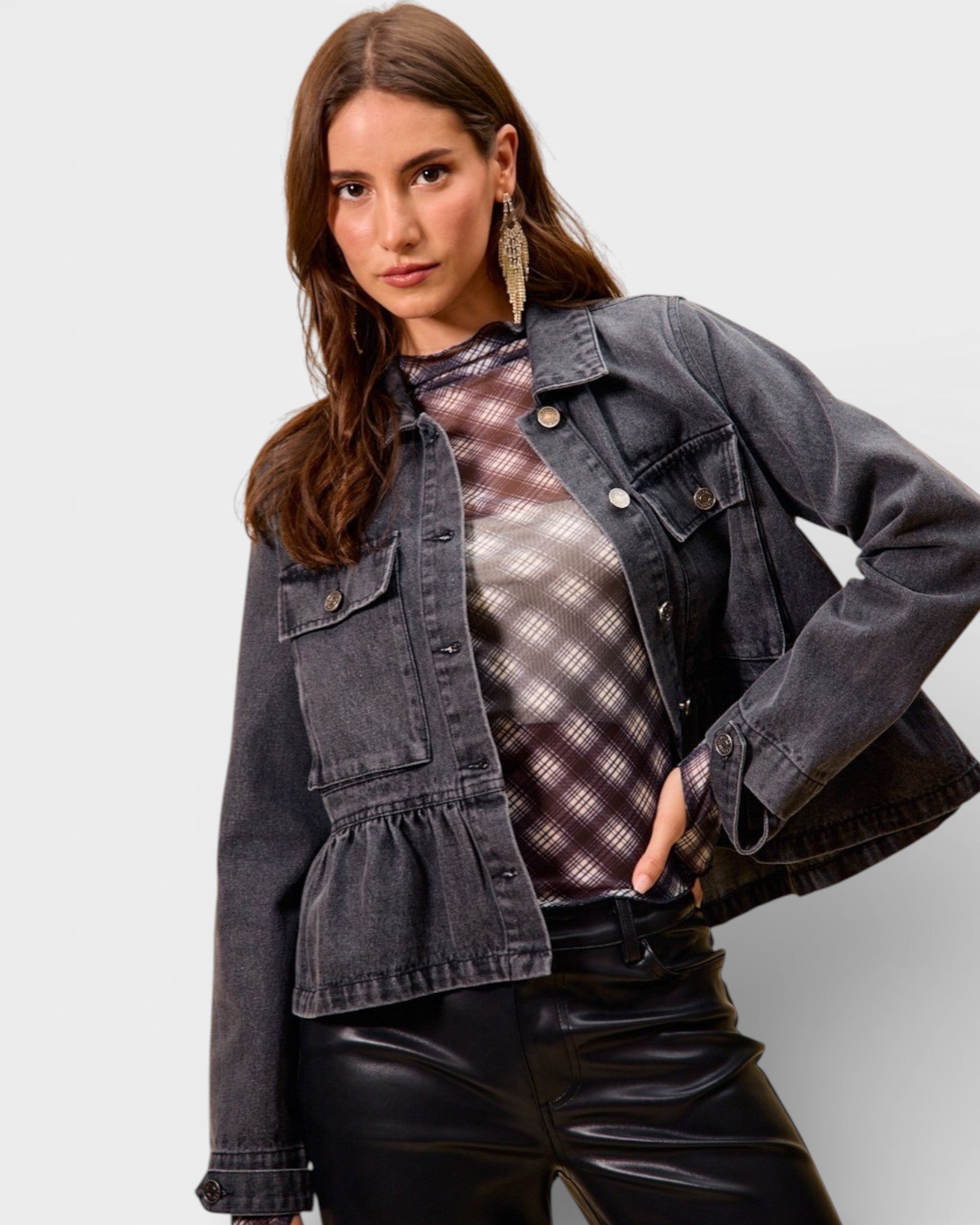Woman wearing a denim jacket over a plaid shirt with a plain background
