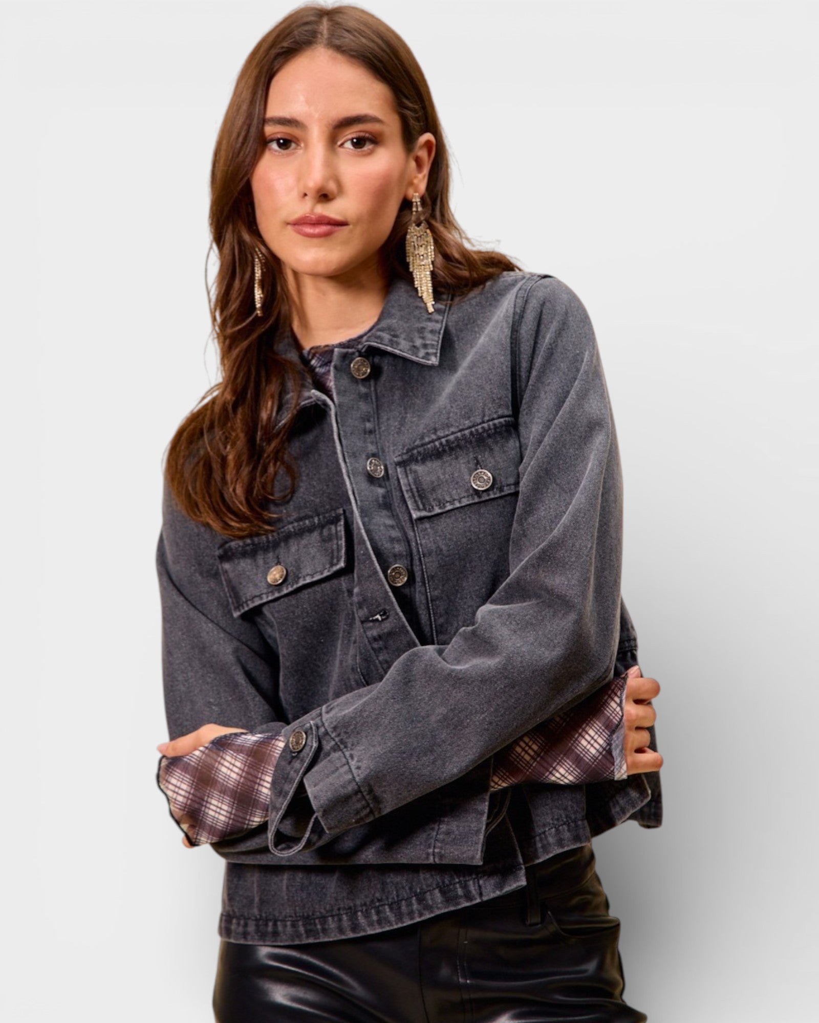 Woman wearing a denim jacket over a plaid shirt with a plain background