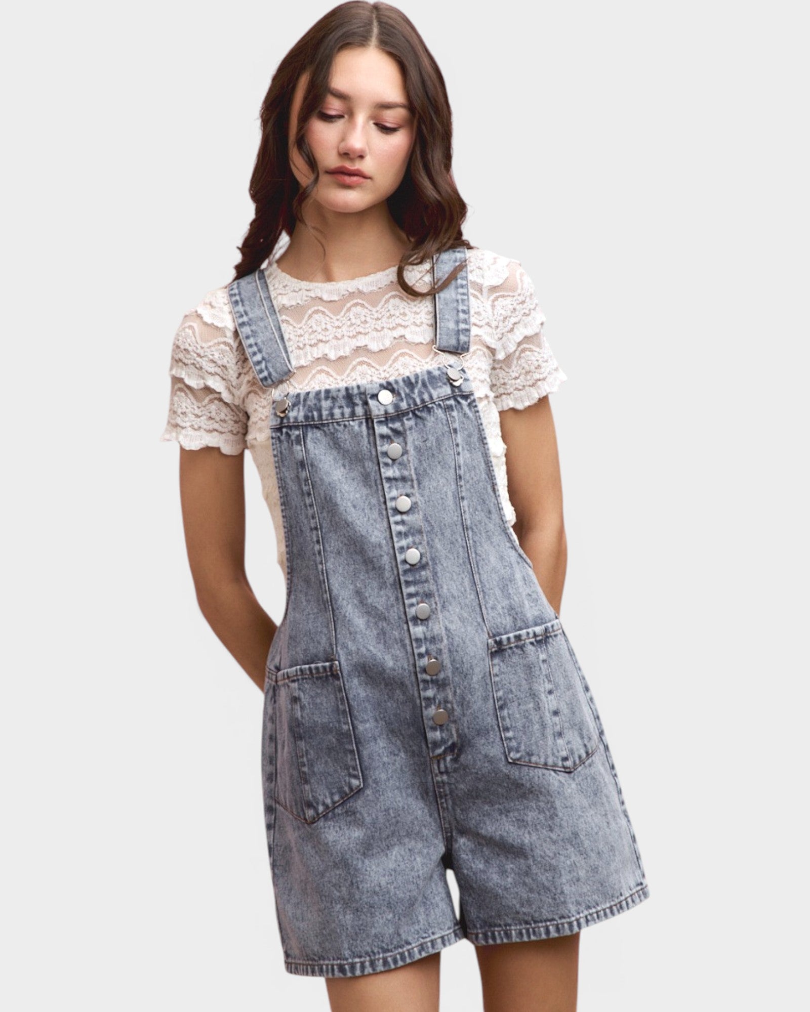Woman wearing denim overalls over a lace top on a plain background