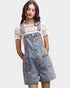 Woman wearing denim overalls over a lace top on a plain background