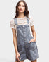 Woman wearing denim overalls over a lace top on a plain background