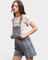 Woman wearing denim overalls over a lace top on a plain background