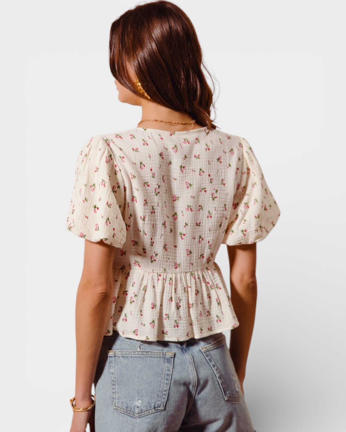 Woman wearing a floral blouse and jeans on a plain background