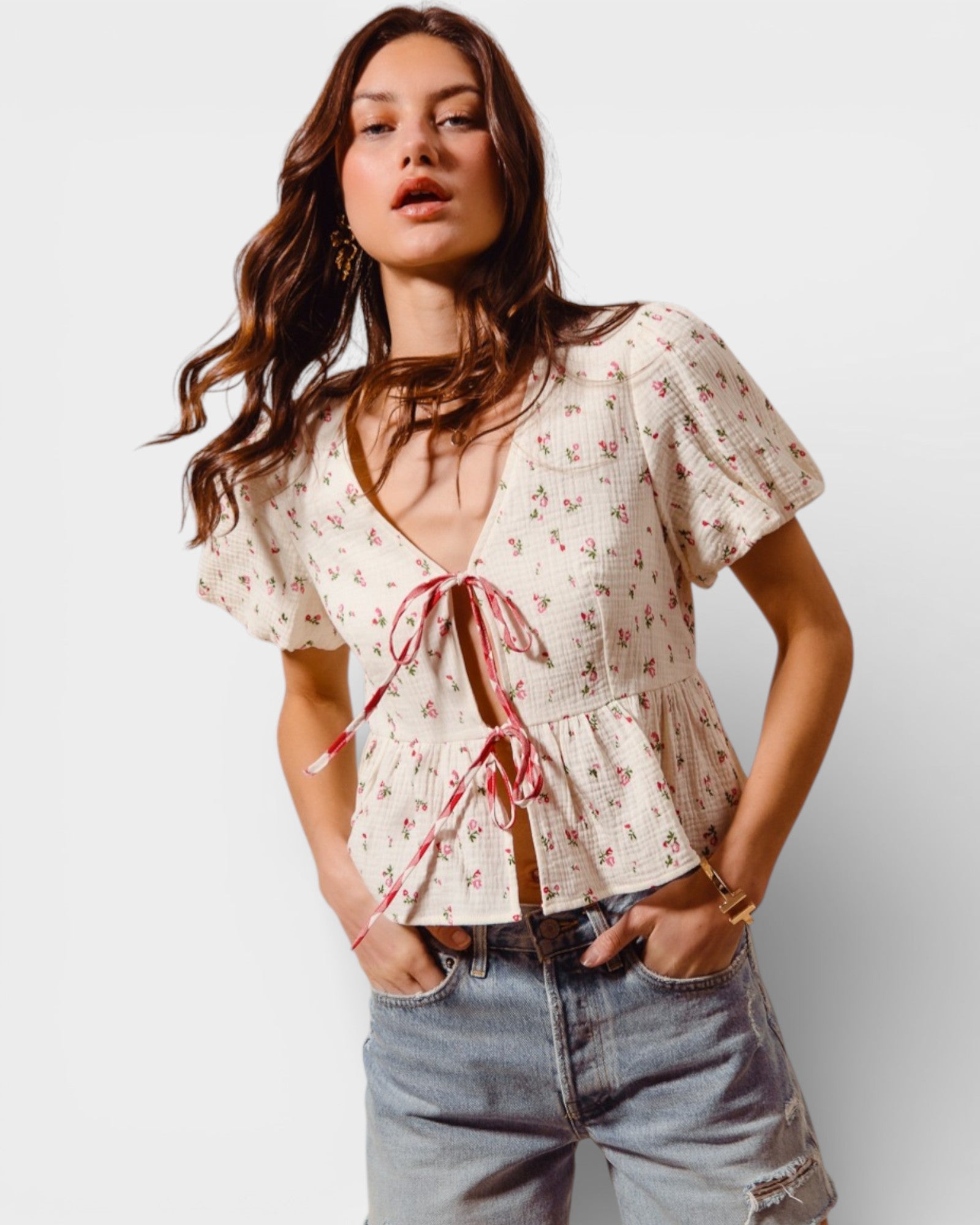 Woman wearing a floral blouse with a tie detail and jeans on a white background