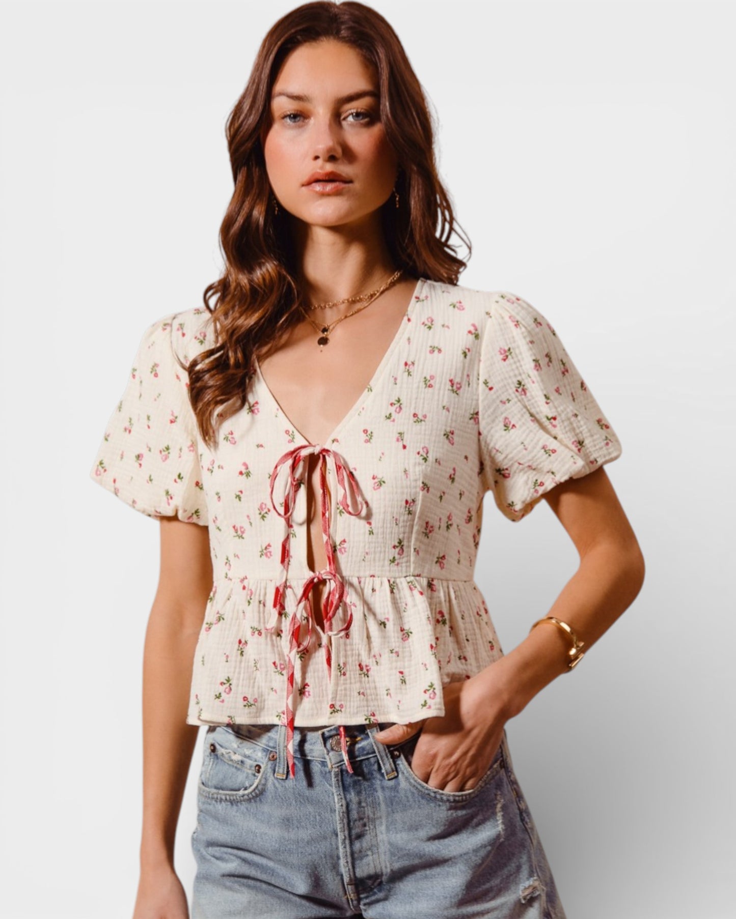 Woman wearing a floral blouse with a tie detail and jeans on a plain background