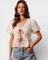 Woman wearing a floral blouse with a tie detail and jeans on a plain background