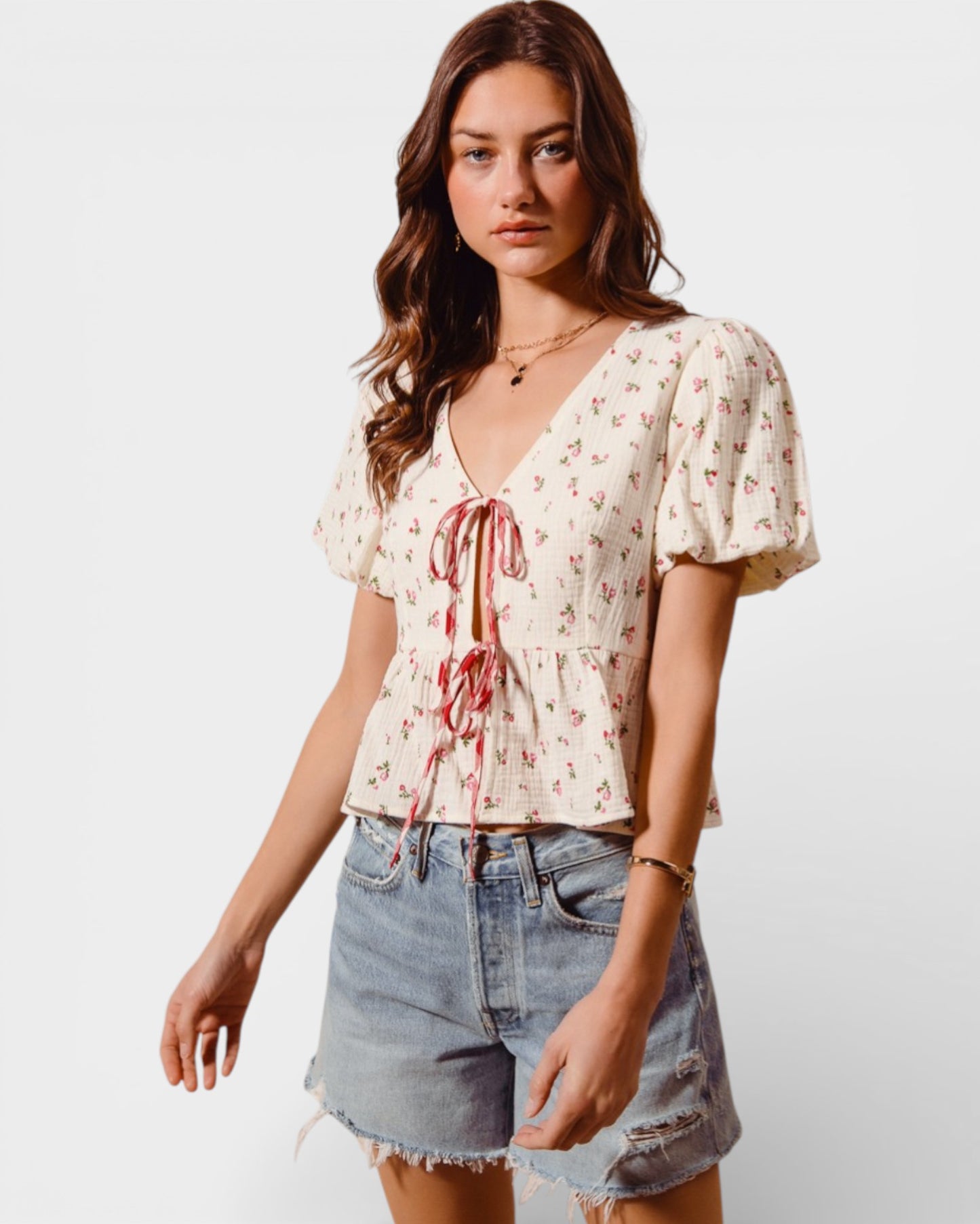 Woman wearing a floral blouse and denim shorts on a white background