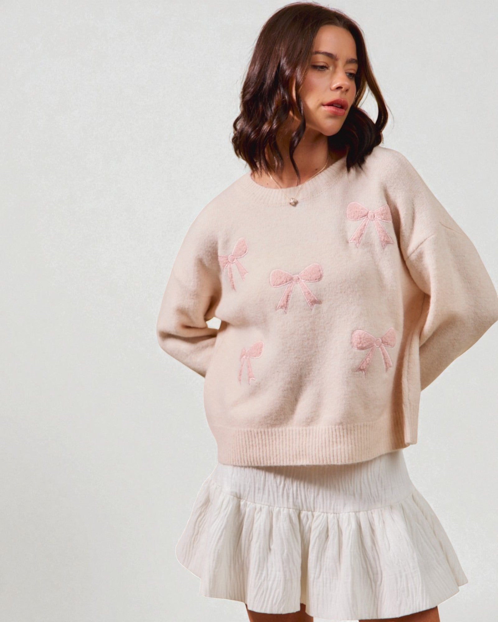 Woman wearing a light pink sweater with bow patterns and a white skirt on a plain background