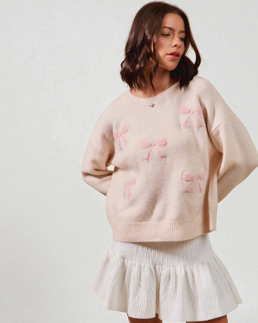 Woman wearing a light pink sweater with bow patterns and a white skirt on a plain background