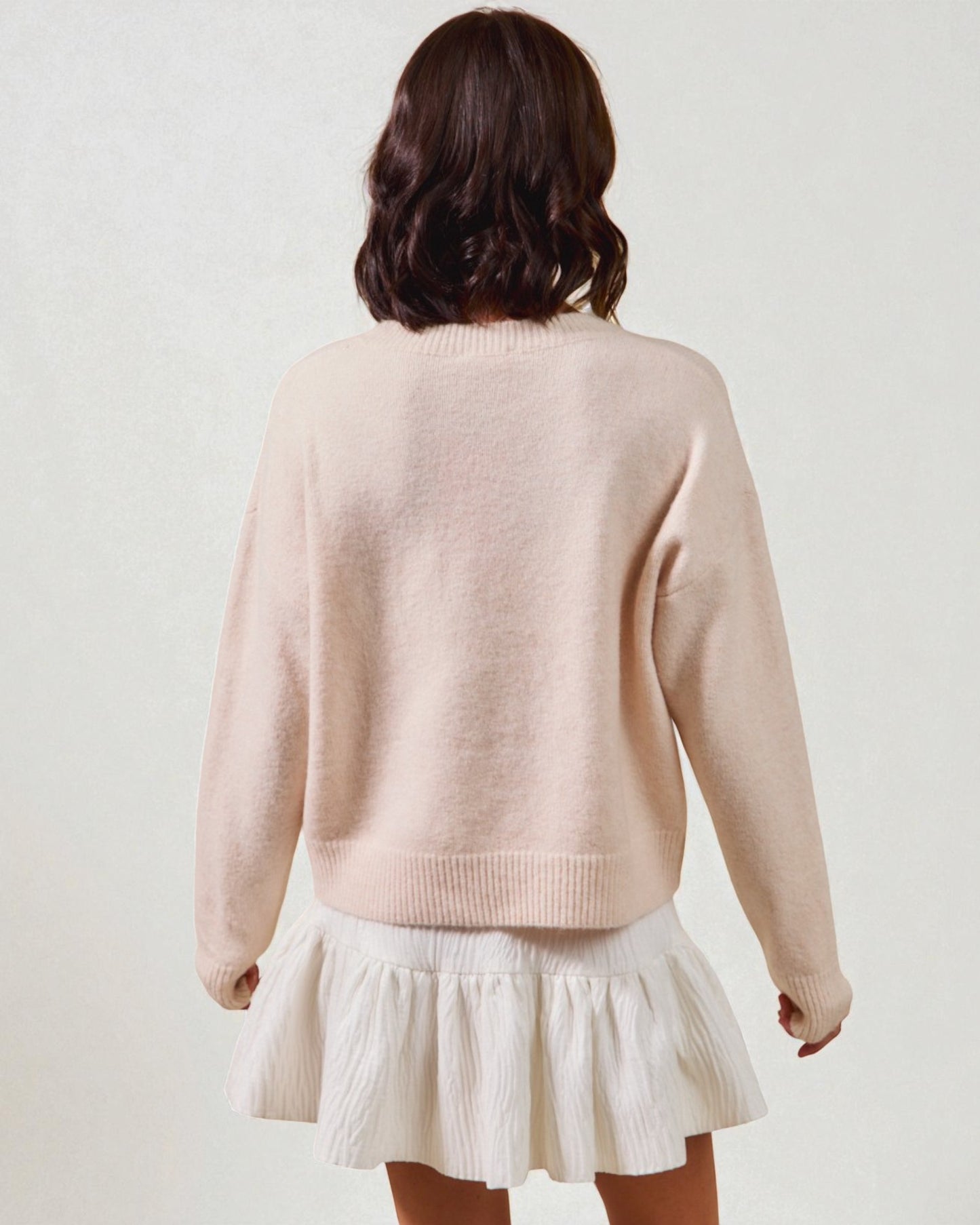 Person wearing a light pink sweater and white skirt on a plain background