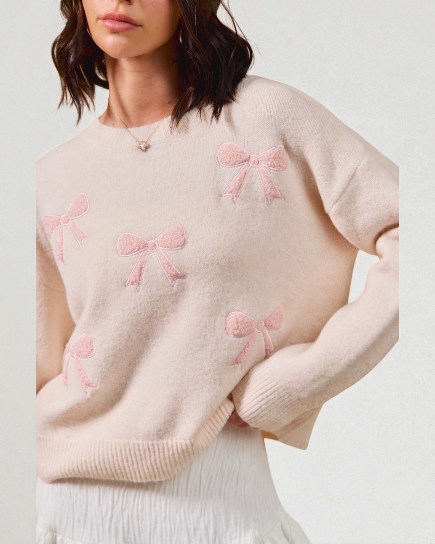 Light pink sweater with bow patterns worn by a person on a plain background