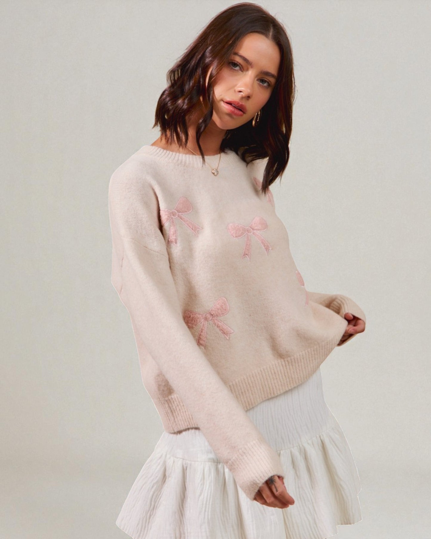 Woman wearing a light pink sweater with floral patterns on a plain background