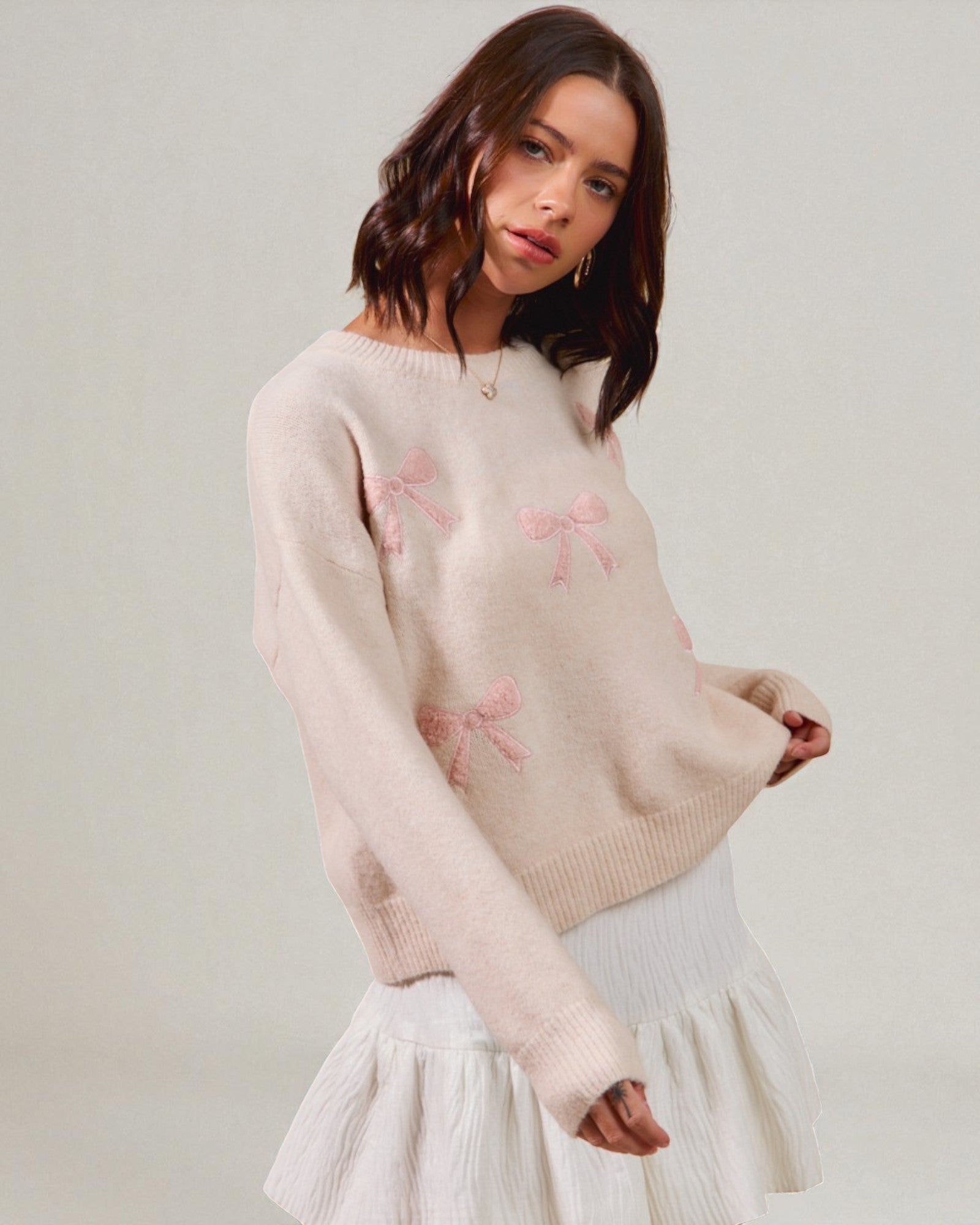 Woman wearing a light pink sweater with floral patterns on a plain background