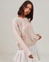 Woman wearing a light pink sweater with floral patterns on a plain background