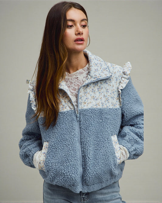 Woman wearing a blue and white fleece jacket with floral pattern on a gray background