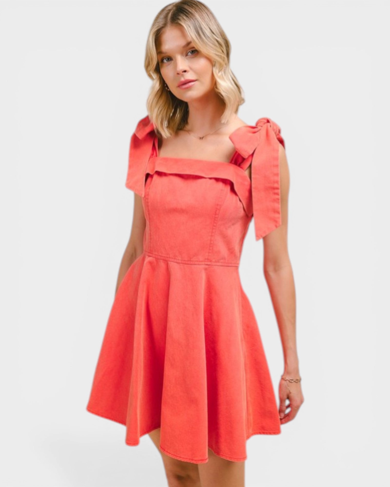 Woman wearing a coral dress with bow details on a white background