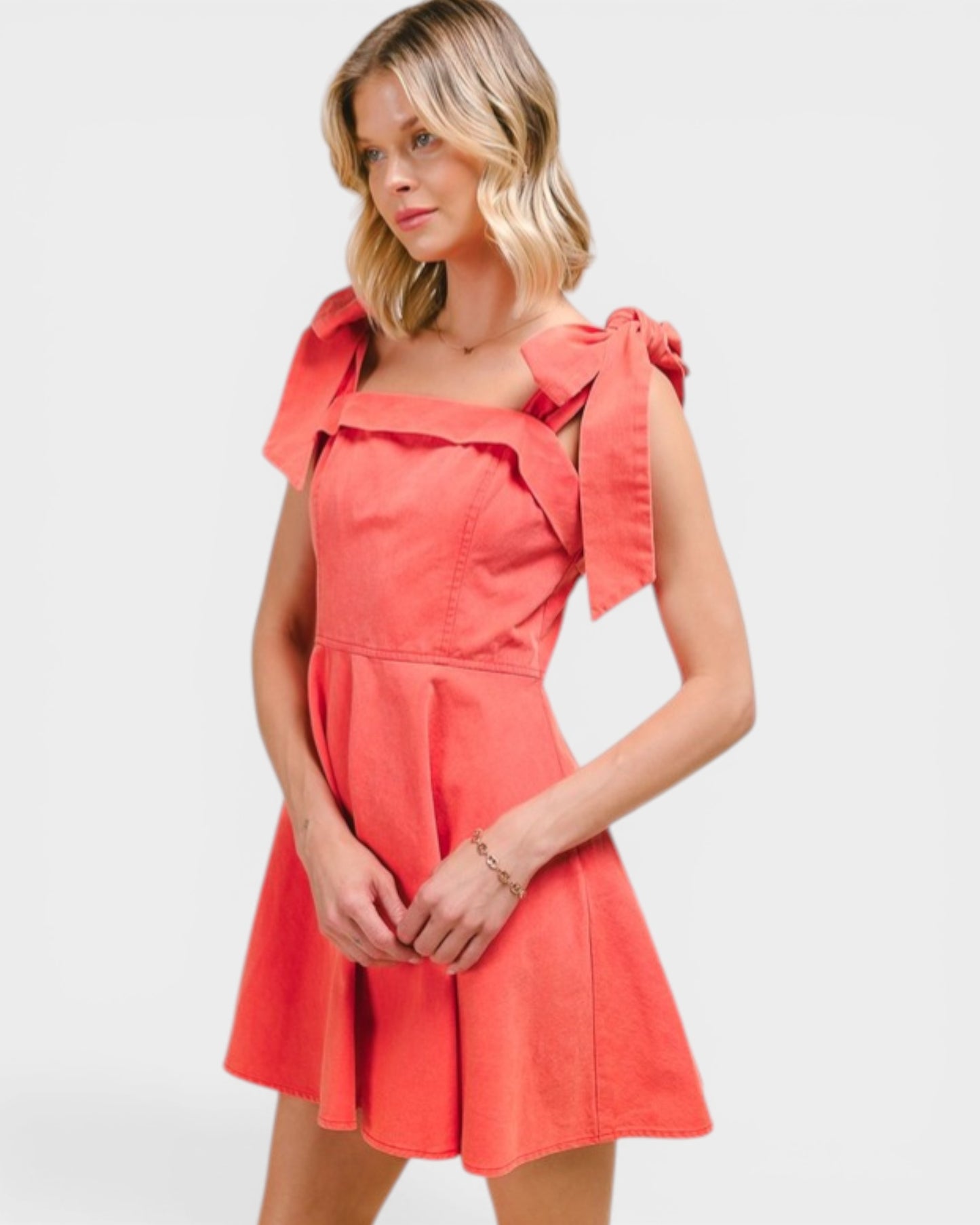 Woman wearing a coral dress with bow details on a white background