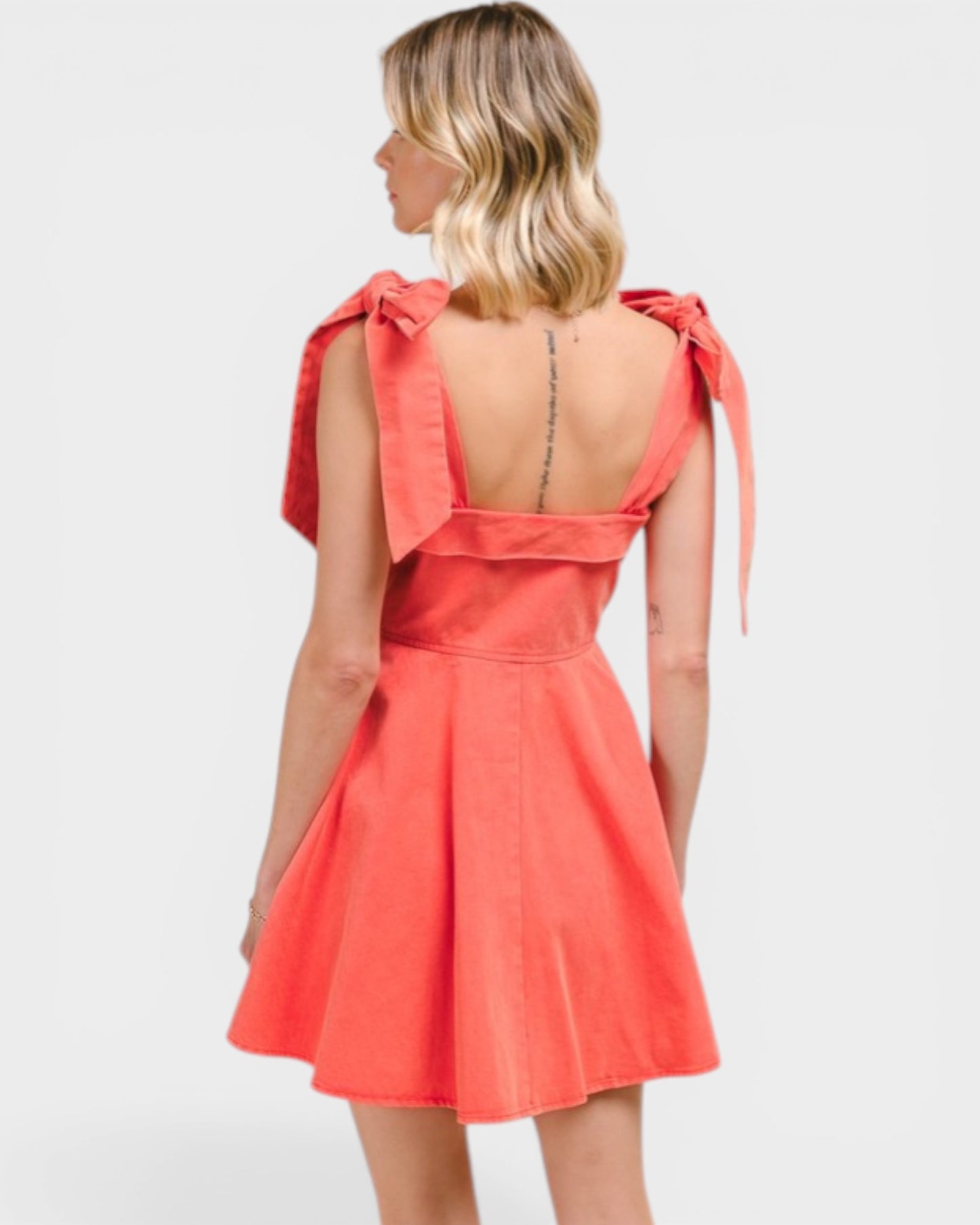 Woman wearing a coral dress with bow straps on a white background