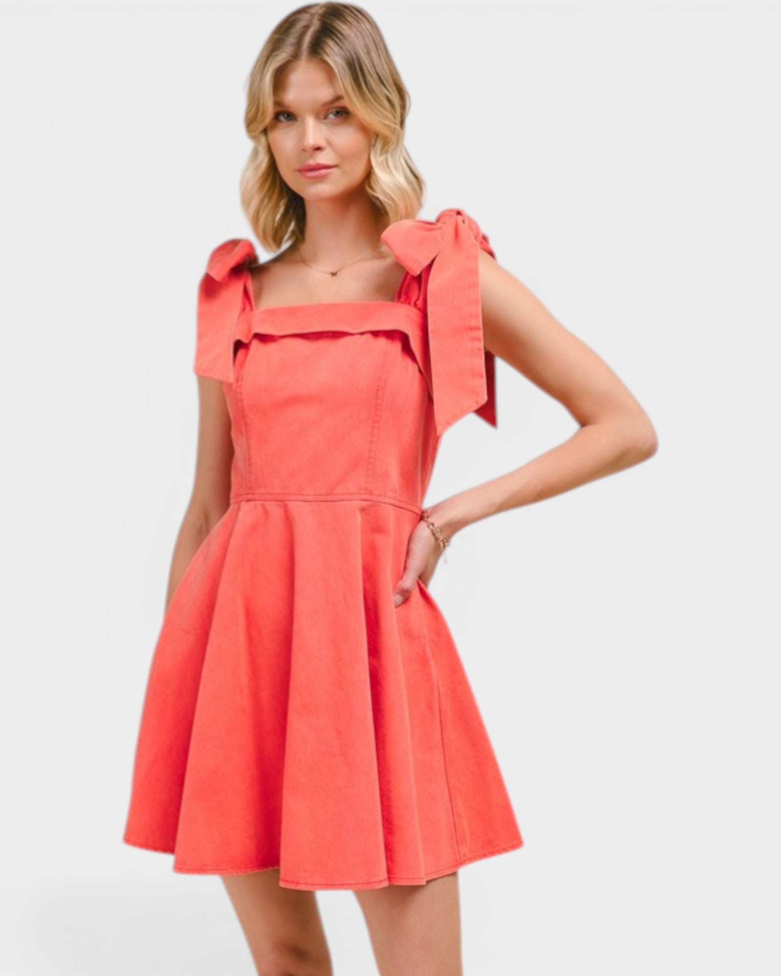 Woman wearing a coral dress with bow straps on a light gray background