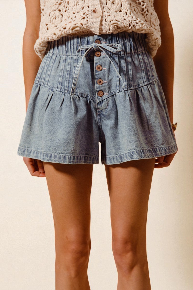 Denim shorts with button details worn by a person on a beige background