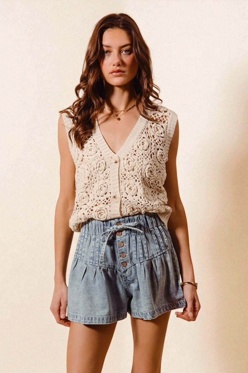 Woman wearing a beige lace top and denim shorts against a beige background