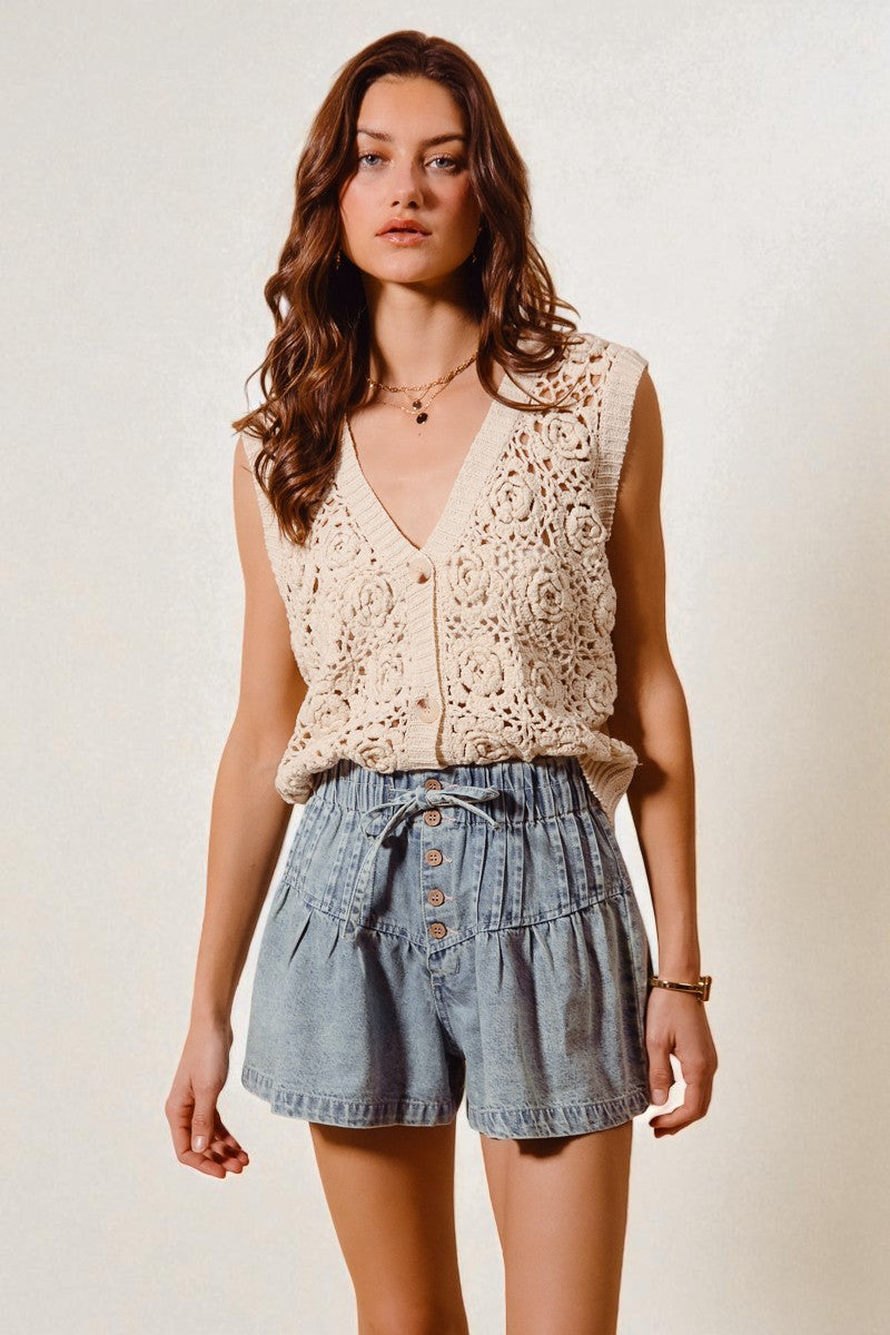 Woman wearing a beige crochet top and denim shorts on a plain background