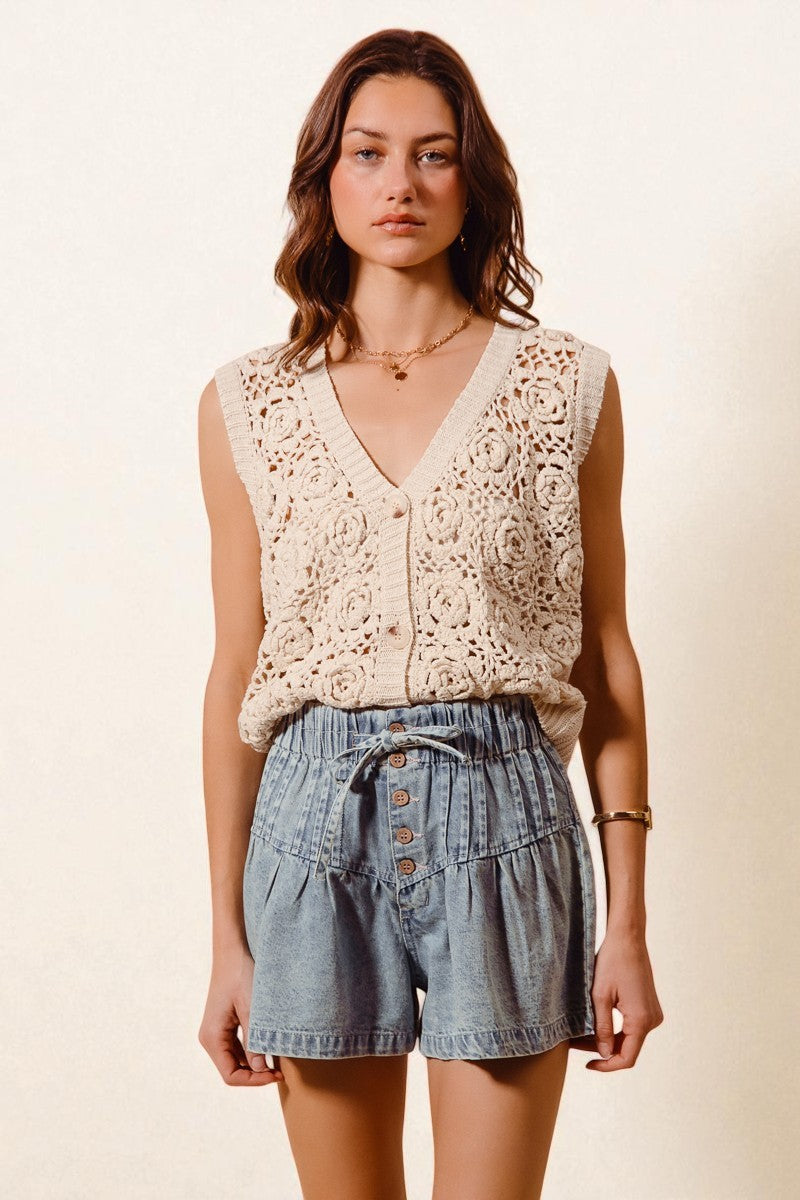 Woman wearing a beige crochet top and denim shorts on a plain background