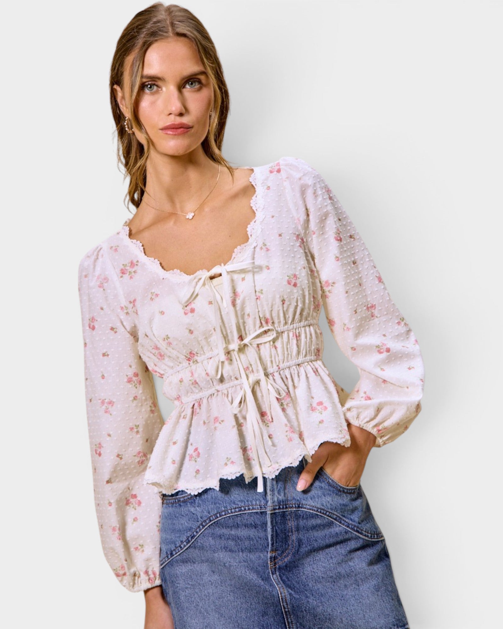 Woman wearing a floral blouse and jeans against a plain background