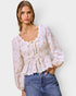 Woman wearing a floral blouse and jeans against a plain background
