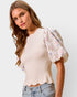 Woman wearing a beige top with floral sleeves and light blue jeans on a plain background