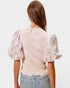 Woman wearing a beige blouse with floral sleeves on a plain background