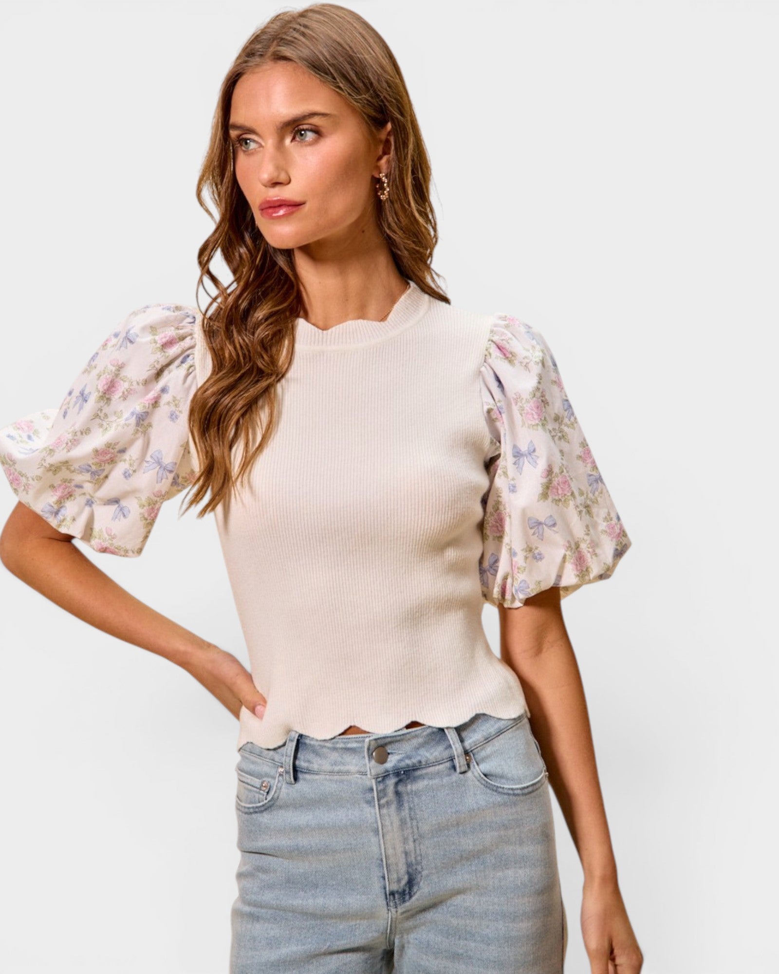 Woman wearing a floral blouse with puffed sleeves and jeans on a plain background