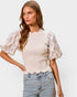 Woman wearing a floral blouse with puffed sleeves and jeans on a plain background