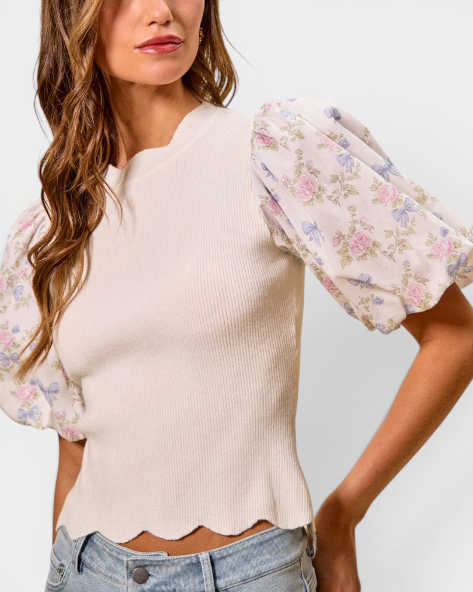 Woman wearing a cream-colored top with floral sleeves on a plain background
