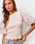 Woman wearing a cream top with floral sleeves against a plain background